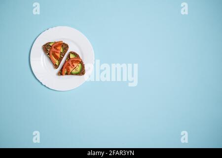 Blick von oben auf ein vegetarisches Sandwich mit Avocado und Tomaten Blauer Hintergrund Stockfoto