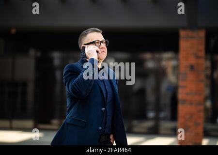 Leitenden Geschäftsmann zu Fuß und mit einem Gespräch am Telefon - Porträt von Reifen zuversichtlich lächelnder Mann, eleganten Anzug Stockfoto
