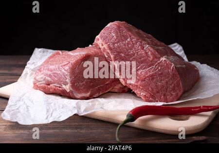 Zwei große Stücke Kalbsfilet, rohes Fleisch auf einem Schneidebrett auf dunklem Holzhintergrund, rustikaler Stil, Nahaufnahme. Stockfoto