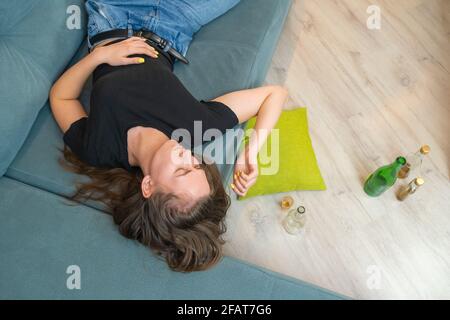 Betrunkene junge dunkelhaarige Frau schläft nach einer Party oder Stress mit leeren Flaschen auf dem Boden auf der Couch, Draufsicht aus dem Kopierraum Stockfoto