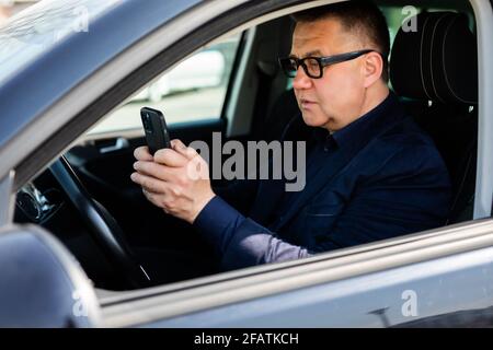Mann mittleren Alters mit seinem Smartphone am Steuer Stockfoto