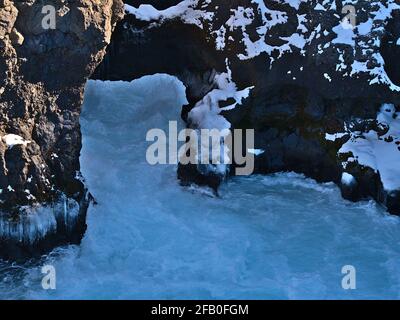 Nahaufnahme des Barnafoss Wasserfalls in einer Schlucht bei der Hraunfossar Kaskade, Húsafell, Westisland an sonnigen Wintertagen mit natürlichem Felsbogen. Stockfoto