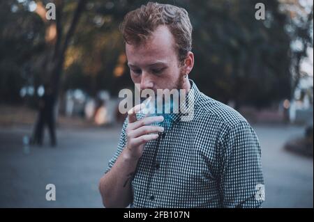 Stilvoller junger bärtiger Mann raucht im Park. Stockfoto