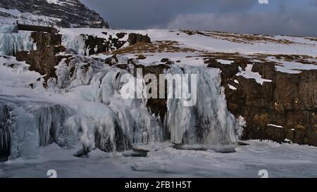 Schöne Aussicht auf den gefrorenen felsigen Wasserfall Kirkjufellsfoss in der Nähe von Grundarfjörður auf der Halbinsel Snæfellsnes, Westisland in der Wintersaison mit Schnee. Stockfoto