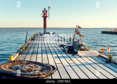 Gefrorener Pier mit Angelzubehör - rote Fahnen, Anker, Netz, Seile und Möwen und rote Seemark an sonnigen Wintertagen Stockfoto