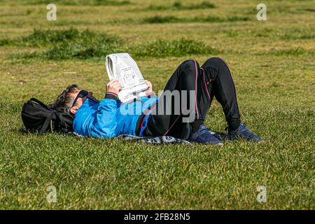 WIMBLEDON LONDON, GROSSBRITANNIEN. 23. April 2021. Ein Mann, der am schönen sonnigen Tag auf dem Wimbledon Common, London, mit einer Zeitung auf dem Rasen liegt, während Prognostiker über das Wochenende mit höheren Temperaturen wärmeres Wetter vorhersagen. Kredit: amer ghazzal/Alamy Live Nachrichten Stockfoto