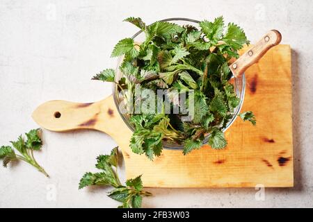 In einer Schüssel auf einem Schneidebrett grüne Brennnesselblätter schneiden. Stockfoto