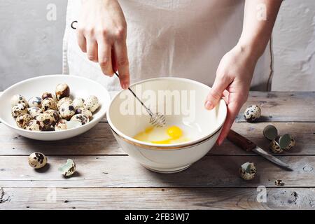 Weibliche Hände peitschten Wachteleier in einer Schüssel an einem Holztisch und machten Mayonnaise. Stockfoto