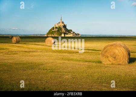 Schöne Aussicht auf die berühmte historische Gezeiteninsel Le Mont Saint-Michel Im schönen goldenen Abendlicht bei Sonnenuntergang im Sommer mit Heuballen auf leerem Fiel Stockfoto