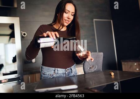 Schöne Brünette Frau gießt sich Rotwein in ihre Küche Stockfoto