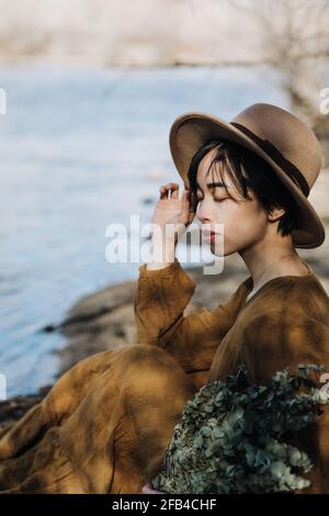 Schöne Frau, die am Flussufer sitzt Stockfoto