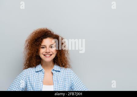 Lockige Frau im karierten Hemd lächelt isoliert auf der Kamera Grau Stockfoto