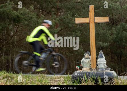 Ein Kreuz am Straßenrand mit Kerzen zum Gedenken an den tragischen Tod, auf einer Fahrt im Hintergrund verschwommen Radfahrer. Stockfoto