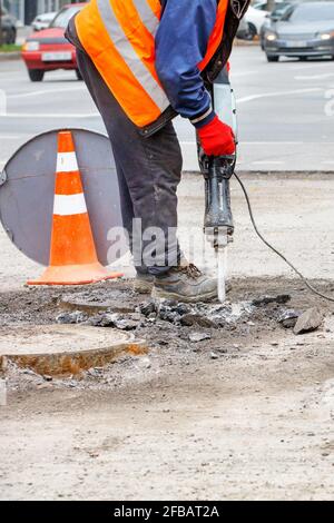 Ein Straßenarbeiter in reflektierender Kleidung arbeitet mit einem Presshammer auf der Fahrbahn und zerschlägt alten Asphalt um Kanalisation. Vertikales Bild, Kopierbereich. Stockfoto