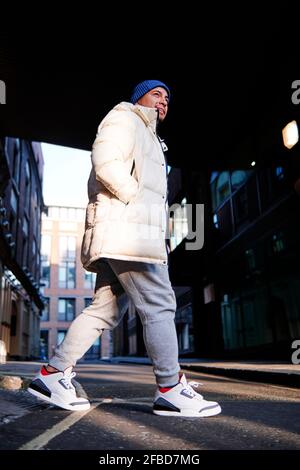 Junger Mann mit Händen in Taschen überqueren Straße auf sonnig Tag Stockfoto