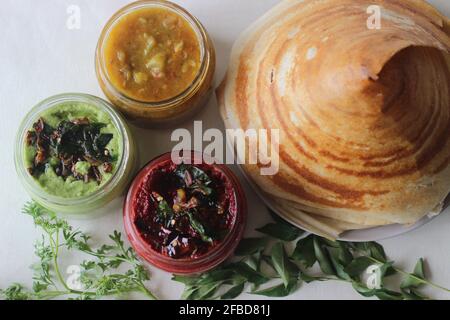 Knuspriger Pfannkuchen aus Reis und Linsen, kegelförmig gefaltet. Serviert mit würzigen Kokosnussgewürzen aus Rote Beete, Koriander-Kokoswürzen und Sambar Stockfoto