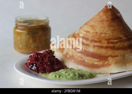 Knuspriger Pfannkuchen aus Reis und Linsen, kegelförmig gefaltet. Serviert mit würzigen Kokosnussgewürzen aus Rote Beete, Koriander-Kokoswürzen und Sambar Stockfoto