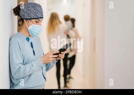 Zahnarzt trägt eine schützende Gesichtsmaske und eine chirurgische Kappe mit Handy Telefon auf dem Flur Stockfoto