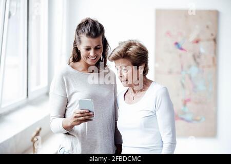 Lächelnde junge Frau, die der Großmutter zu Hause das Mobiltelefon zeigt Stockfoto
