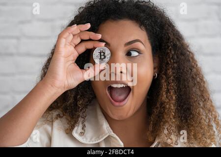 Aufgeregte Frau mit offenem Mund, das Auge mit Bitcoin vor der Wand bedeckt Stockfoto