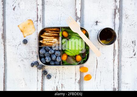 Lunchbox mit Salat, Avocado und gelben Tomaten, Crackern, Blaubeeren und Salatdressing Stockfoto