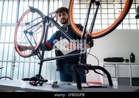 Mann mit digitalem Tablet, der zu Hause Fahrrad hält Stockfoto