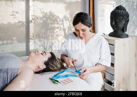 Weibliche Physiotherapeutin schneidet elastisches therapeutisches Klebeband am Tisch ein Klinik Stockfoto