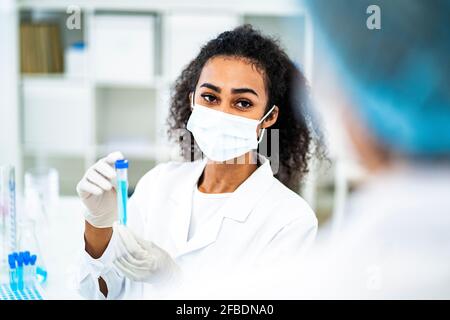 Forscherin, die das Reagenzglas hält, während sie ihre Kollegin anschaut Labor während der COVID-19 Stockfoto