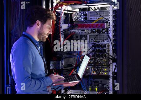 Männlicher IT-Spezialist, der an einem Laptop im Serverraum arbeitet Stockfoto