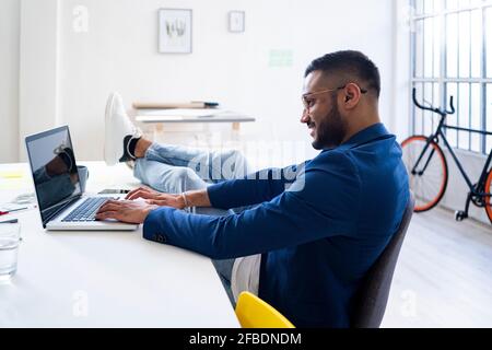 Entspannter Geschäftsmann, der in einem modernen Büro am Laptop arbeitet Stockfoto