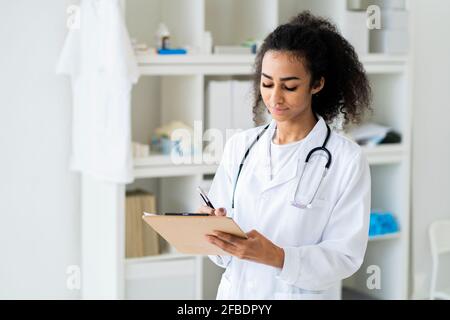 Junge Ärztin, die während der Arbeit in der Klinik auf die Zwischenablage schreibt Stockfoto