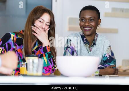 Lächelnde Kolleginnen, die in der Cafeteria am Tisch sitzen Stockfoto