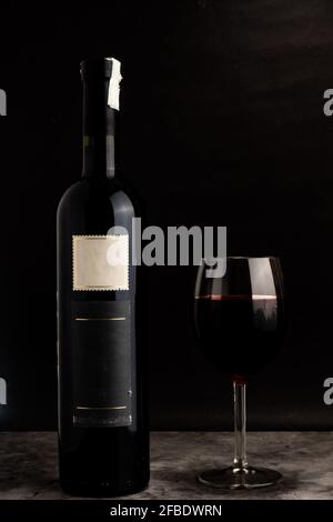 Eine Flasche Wein ohne Namen und ein Glas Wein mit schönem schwarzen Hintergrund, wie im kommerziellen Weinkonzept Stockfoto