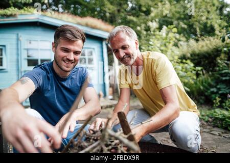 Sohn und Vater arrangieren Feuerholz, während sie im Hinterhof hocken Stockfoto