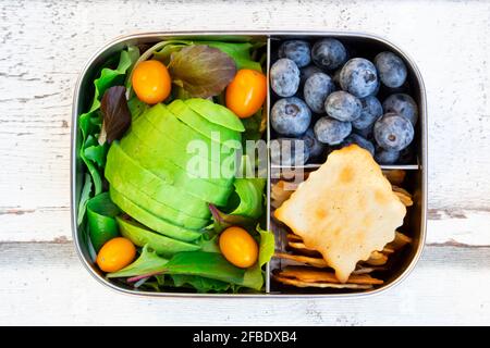 Lunchbox mit Salat, Avocado und gelben Tomaten, Crackern und Heidelbeeren Stockfoto