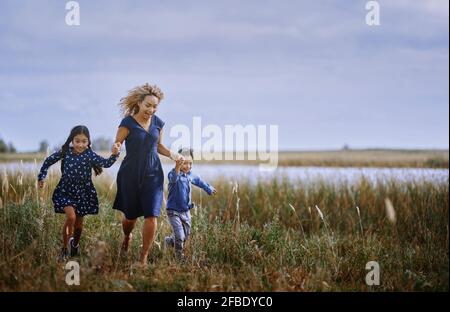 Mutter hält sich die Hände, während sie mit Tochter und Sohn auf Gras läuft Stockfoto
