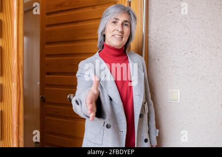 Lächelnde Frau in der Jacke, die vor der Tür des Handschlag anbot Haus Stockfoto