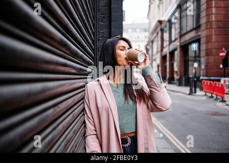 Schöne Frau in Mantel trinken Kaffee, während sie geschlossen stehen Verschluss in der Stadt Stockfoto
