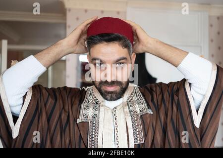 Mann in traditioneller Kleidung trägt Kopfbedeckung zu Hause Stockfoto