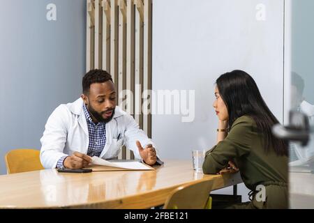 Männlicher Arzt erklärt junge weibliche Patientin über die Krankenakte bei Klinik Stockfoto