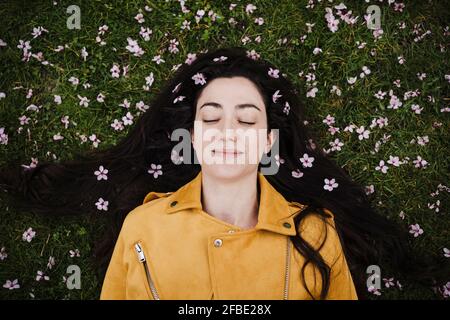 Entspannte Frau mit Blumen im Haar, die auf Gras liegen Stockfoto