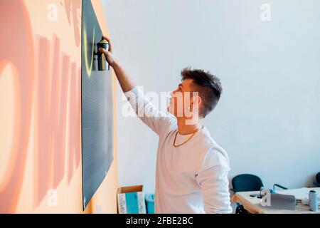 Junger Mann, der im Studio Farbe auf schwarzen Karton sprüht Stockfoto