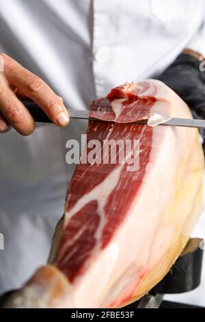 Männlicher Metzger, der Schinken mit Messer schneidet Stockfoto