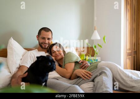 Glückliches Paar mit Pug Hund liegt auf dem Bett zu Hause Stockfoto