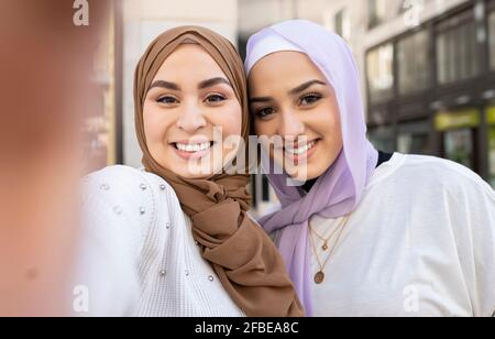 Lächelnde arabische Freundinnen in Hijabs, die in der Stadt Selfie machen Stockfoto