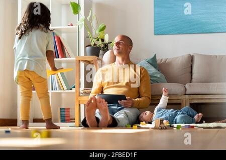 Vater mit digitalem Tablet, der das Kleinkind anschaut, während das Baby liegt Von ihm zu Hause Stockfoto