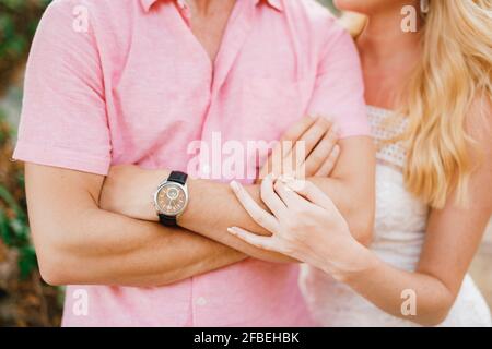 Ein Mann in einem pinken Hemd kreuzte seine Arme über seine Brust, eine blonde Frau umarmte ihn sanft am Ellbogen, aus nächster Nähe Stockfoto