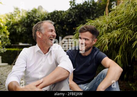 Vater und Sohn lachen, während sie im Hinterhof sitzen Stockfoto