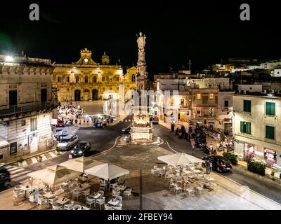 Italien, Provinz Brindisi, Ostuni, Säule des Heiligen Orontius, die nachts auf dem beleuchteten Stadtplatz steht Stockfoto