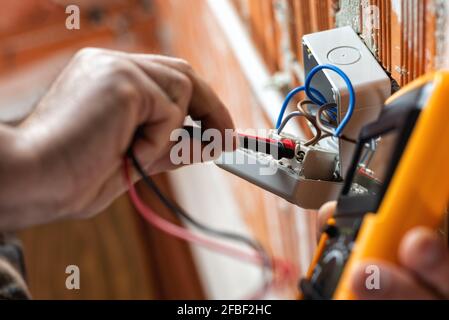 Ansicht von unten. Elektriker bei der Arbeit mit dem Tester misst die Spannung in einem elektrischen System. Bauindustrie. Stockfoto